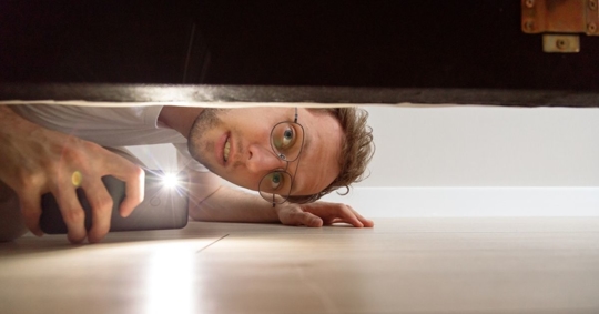Man with flashlight looking under the bed